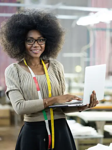 Woman with measuring tape around her neck holding a laptop.