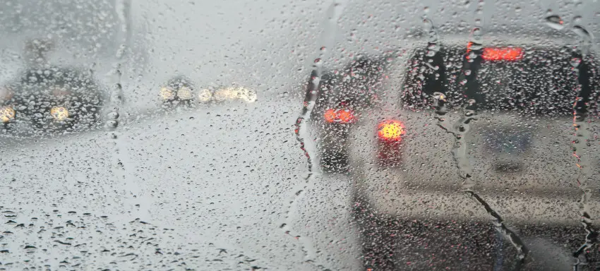White car driving down a highway in the rain. The rain is falling heavily and making it difficult to see