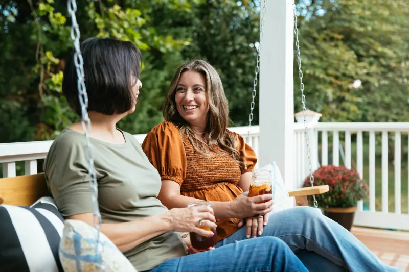 Two women holding iced tea in cups and sitting on front porch swing