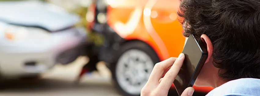 Man using phone to call insurance company after car accident. Orange car and white car involved in collision with damage in background