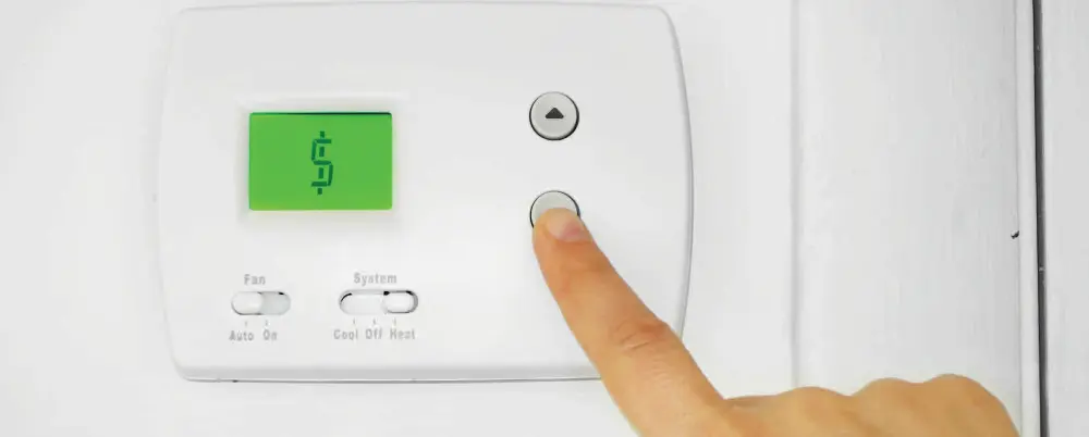 Person adjusting thermostat on the wall in home. Green dollar sign in place of temperature on thermostat to symbolize cost of AC