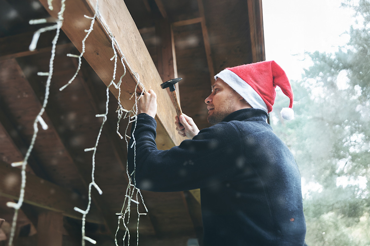 Homeowner on ladder safely decorating his home with lights for Christmas