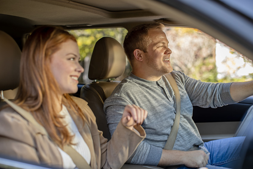 Man and woman riding in car together while wearing seatbelts