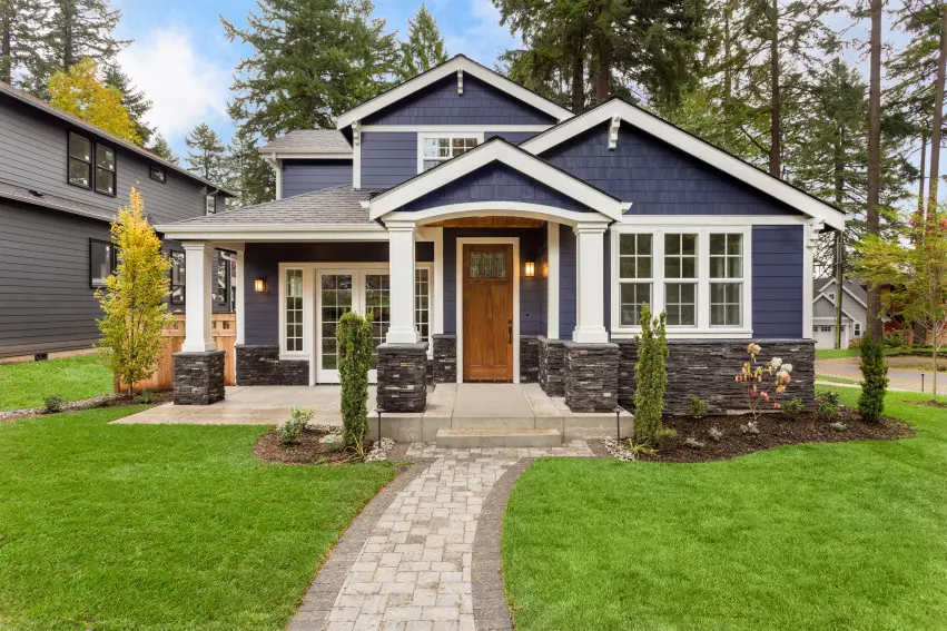 Blue and white craftsman house with a lush green lawn and a brick sidewalk