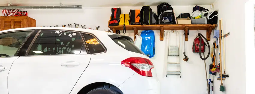 White car parked in home garage that is lined with shelves of organized home items and tools