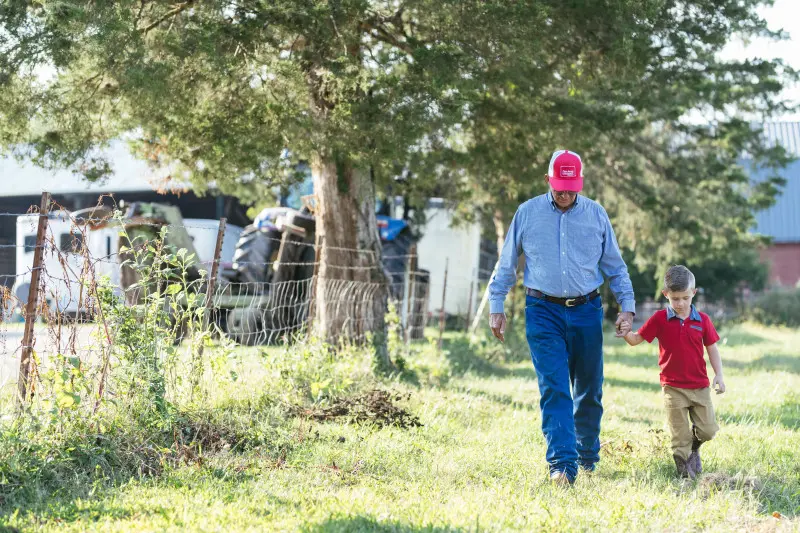 Tennessee farmer walking on a farm while holding hands with his young grandson