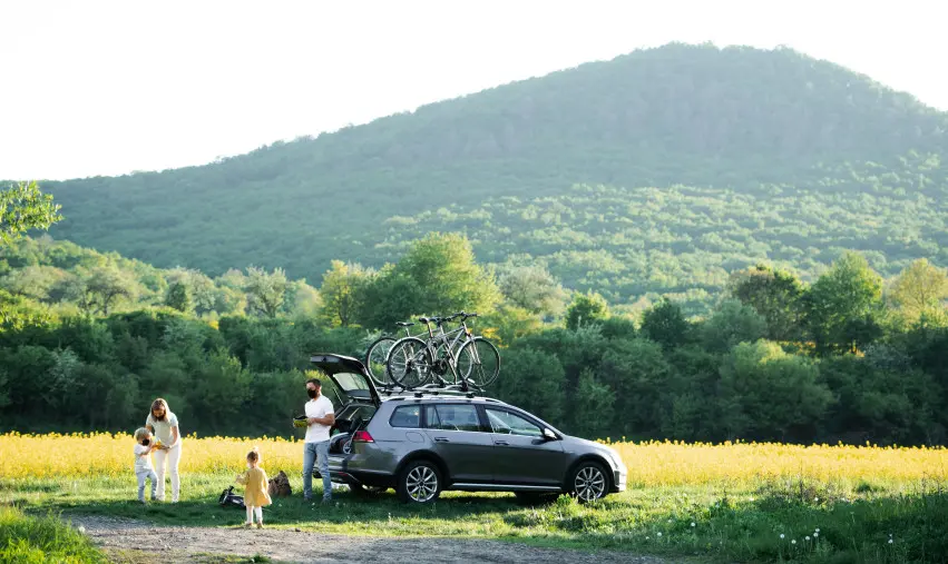 Parents with two young children standing next to their car that is loaded with two bikes on the top