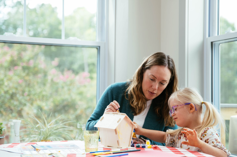 Mother painting birdhouse with her daughter at a table