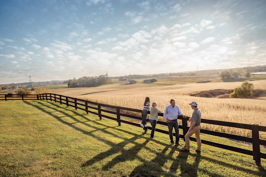 Tennessee family meeting with a Farm Bureau Insurance of Tennessee agent while leaning against the fence on their family farm