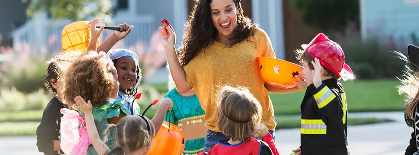 Woman handing out halloween candy to kids in neighborhood who are dressed in halloween costumes