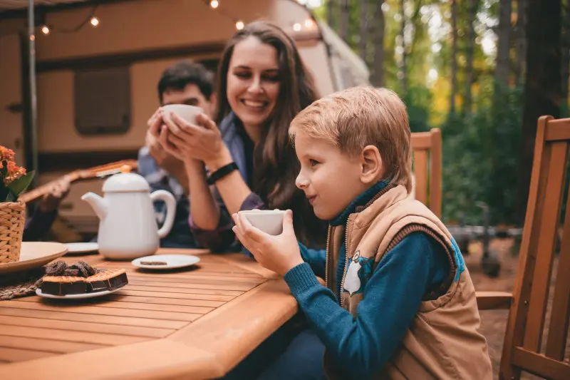 Young boy sips a hot beverage while sitting around a table with his family at a rv campground