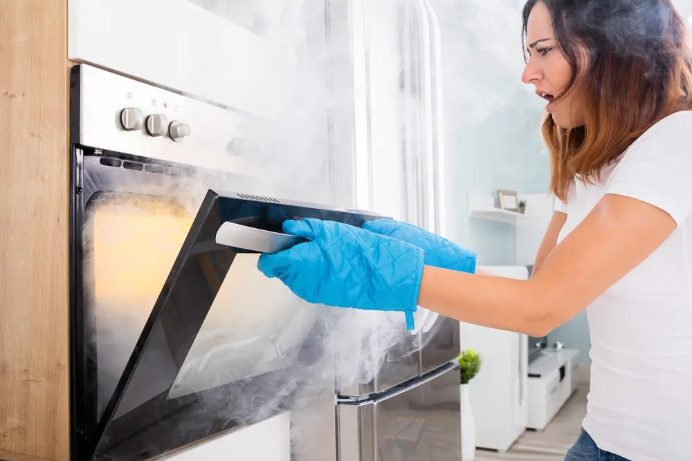 Woman wearing blue oven mitts removing burning item