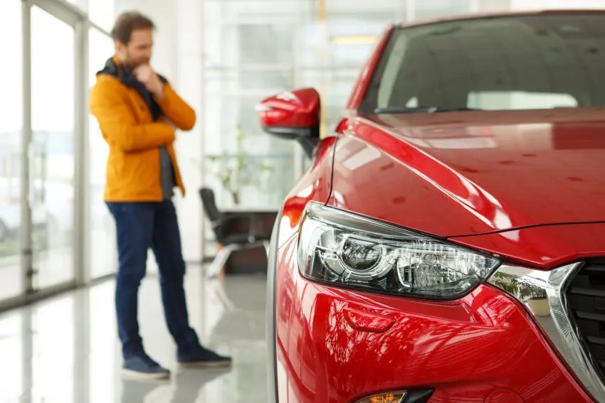 Man inspecting red car on showroom floor of car dealership. Man is contemplating leasing the red car