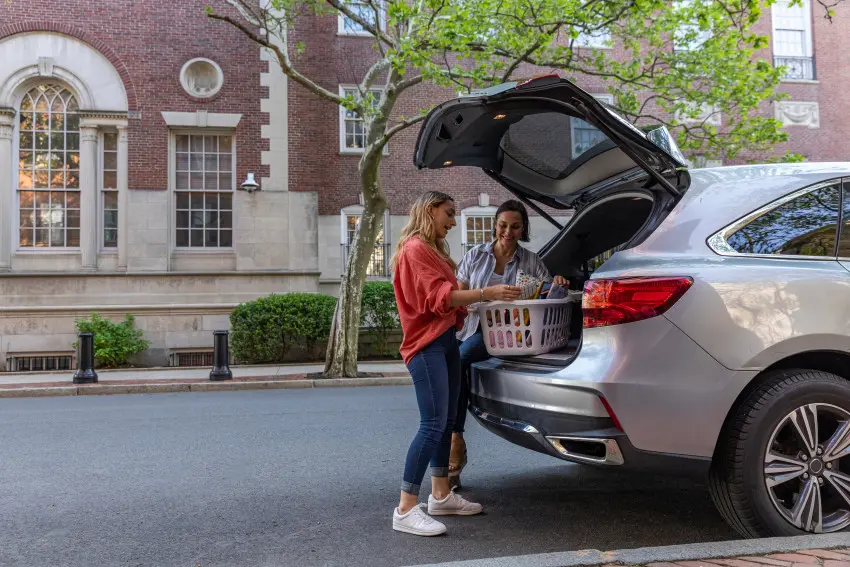 Mother helping her college student daughter unpack a laundry basket of items for college. Unpacking basket from silver car in front of college dorm