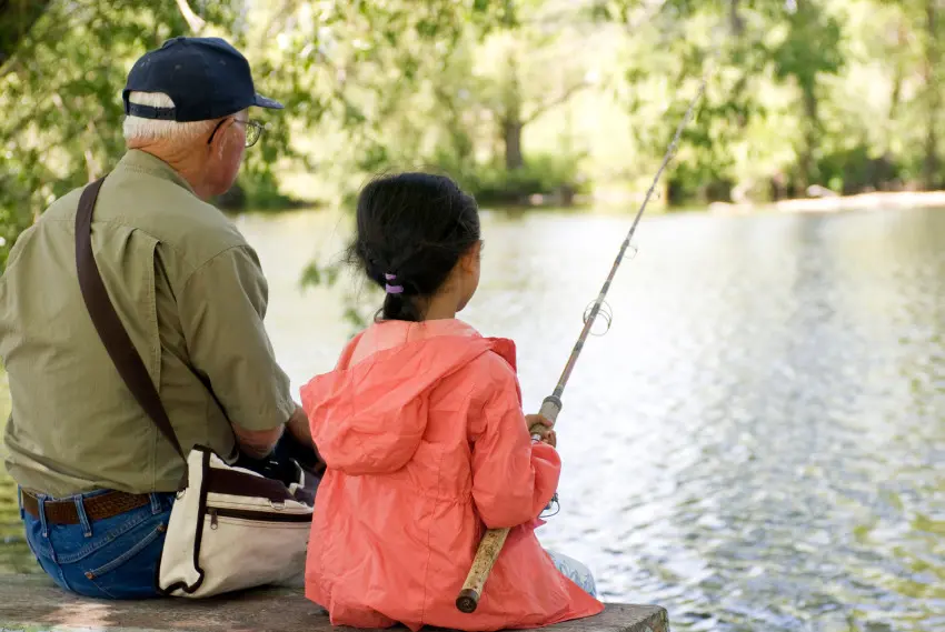 Young girl fishing with grandfather on bank of water