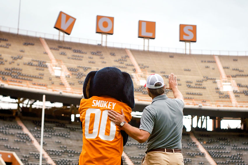 Farm Bureau Insurance of Tennessee agent showing Smokey, the Tennessee Vols mascot, the damage to his sign at Neyland Stadium