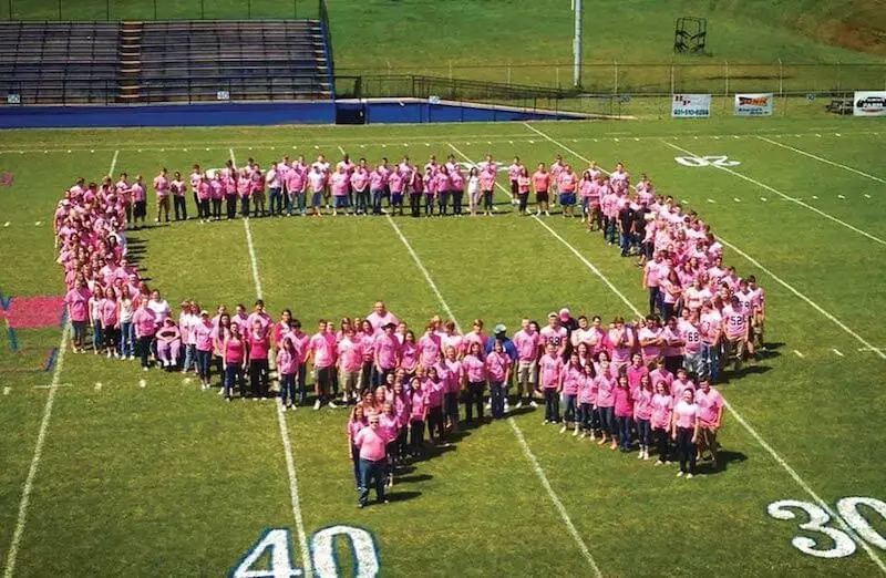 People forming the shape of a Breast Cancer Awareness ribbon on a football field