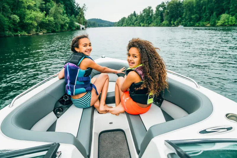 Two young girls wearing lifejackets smiling while riding on a boat on a Tennessee lake