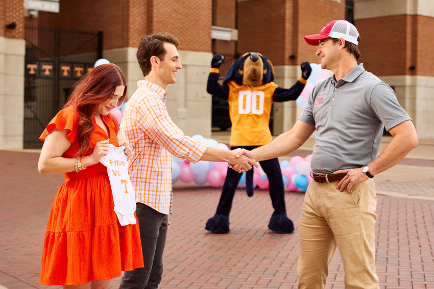 Young couple doing a gender reveal with the Tennessee Vols mascot, Smokey, and a Farm Bureau Insurance of Tennessee agent