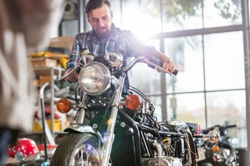 Man with beard and flanel shirt inspecting old motorcycle in auto shop