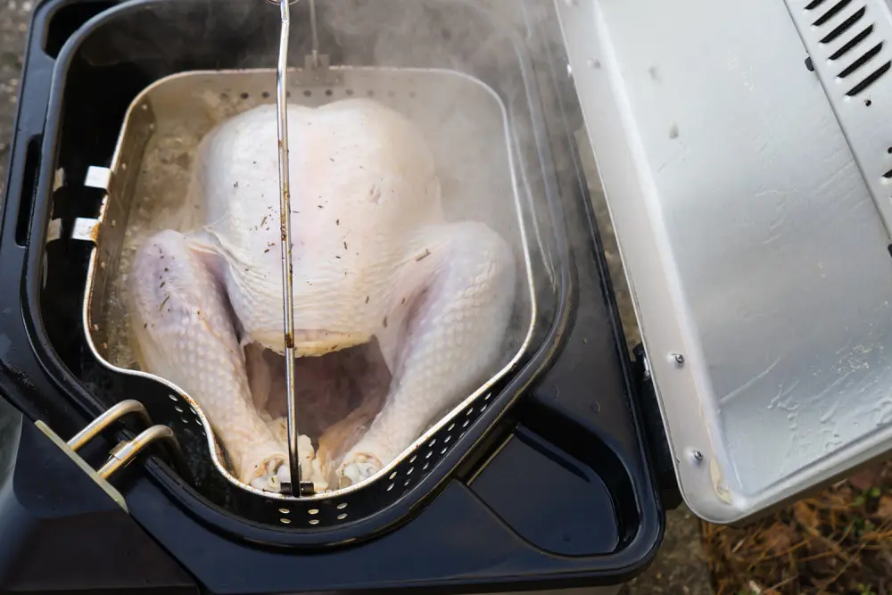 Frozen turkey sitting in fryer submerged in boiling hot grease