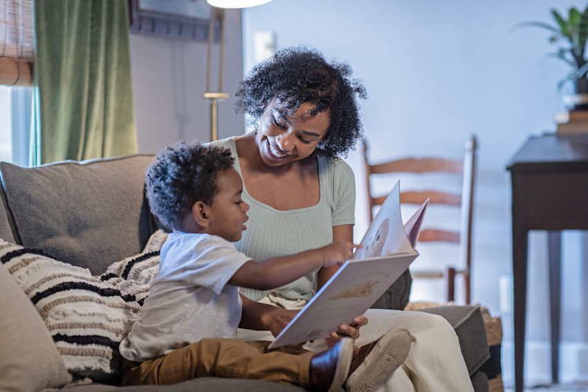 Mother reading a book to her young son on the couch in their home living room