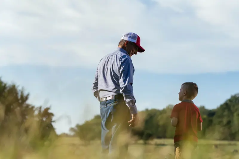 Tennessee farmer smiling while looking down at grandson in field on farm