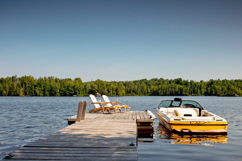 Boat on lake tied up to a dock with two chairs