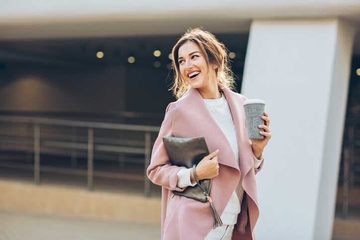 Elegancka kobieta spaceruje w różowym płaszczu z kubkiem kawy