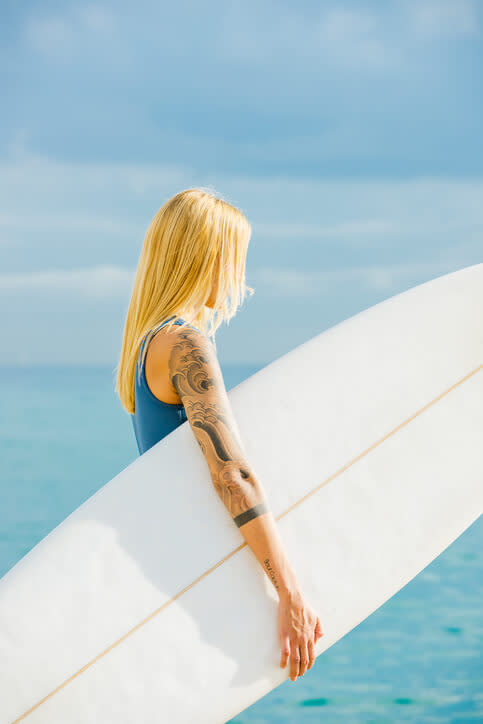Blondynka z tatuażami na ręce trzyma deskę surfingową