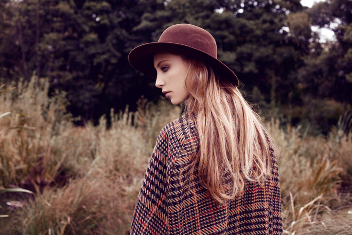 Romantyczna dziewczyna na łące w brązowym płaszczu w kratę i kapeluszu