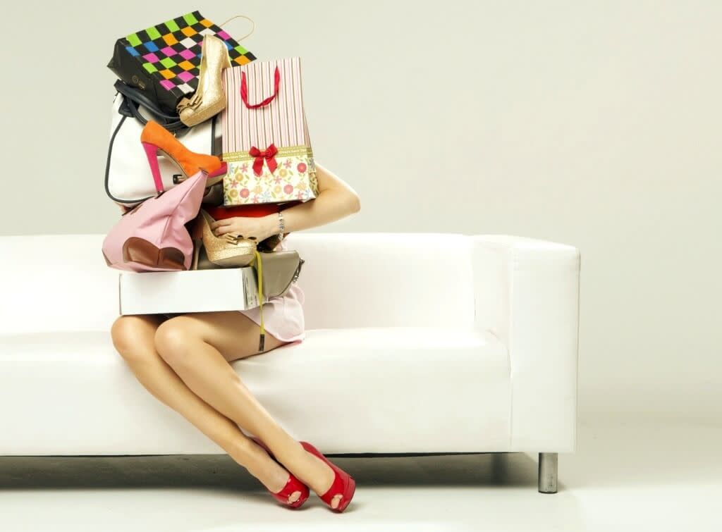 Kobieta siedzi na kanapie trzymając ogromne zakupy