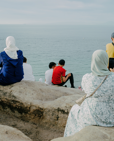 A group of people sit on a rock overlooking the sea.