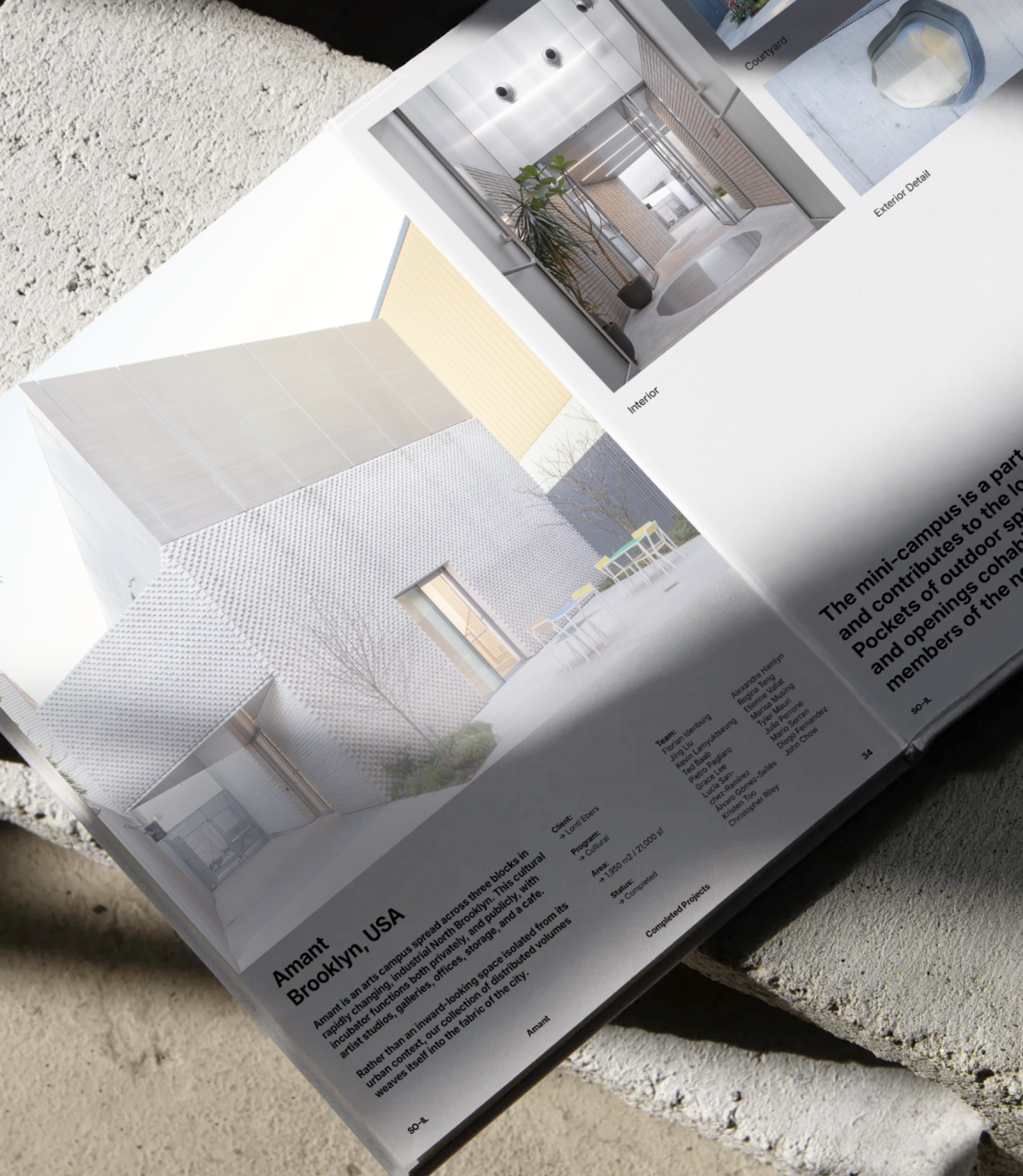 A magazine lies open on concrete blocks, displaying photos and text about Amant in Brooklyn, USA. The page features images of modern architecture with light-colored walls and a minimalist outdoor area.