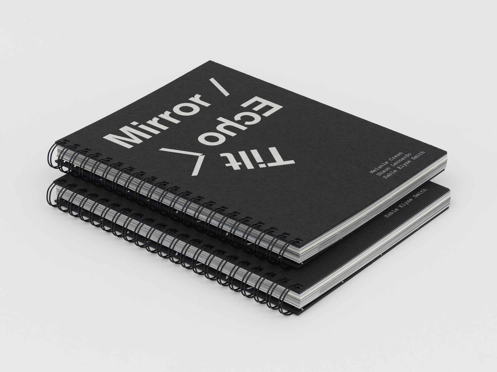 Two black ring-bound books with white title text are stacked on top of each other.