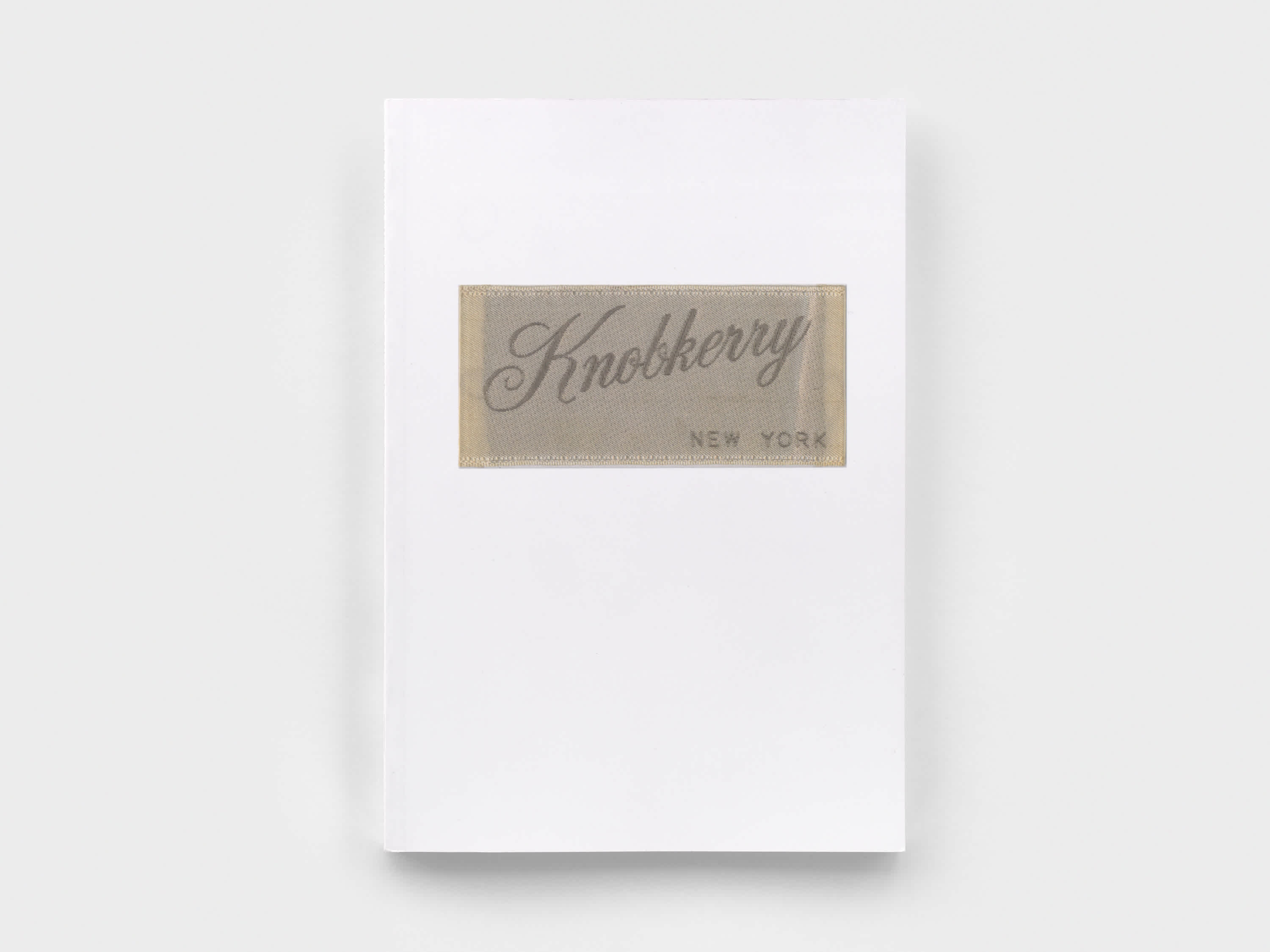 White book cover with enlarged beige clothing tag as the title.