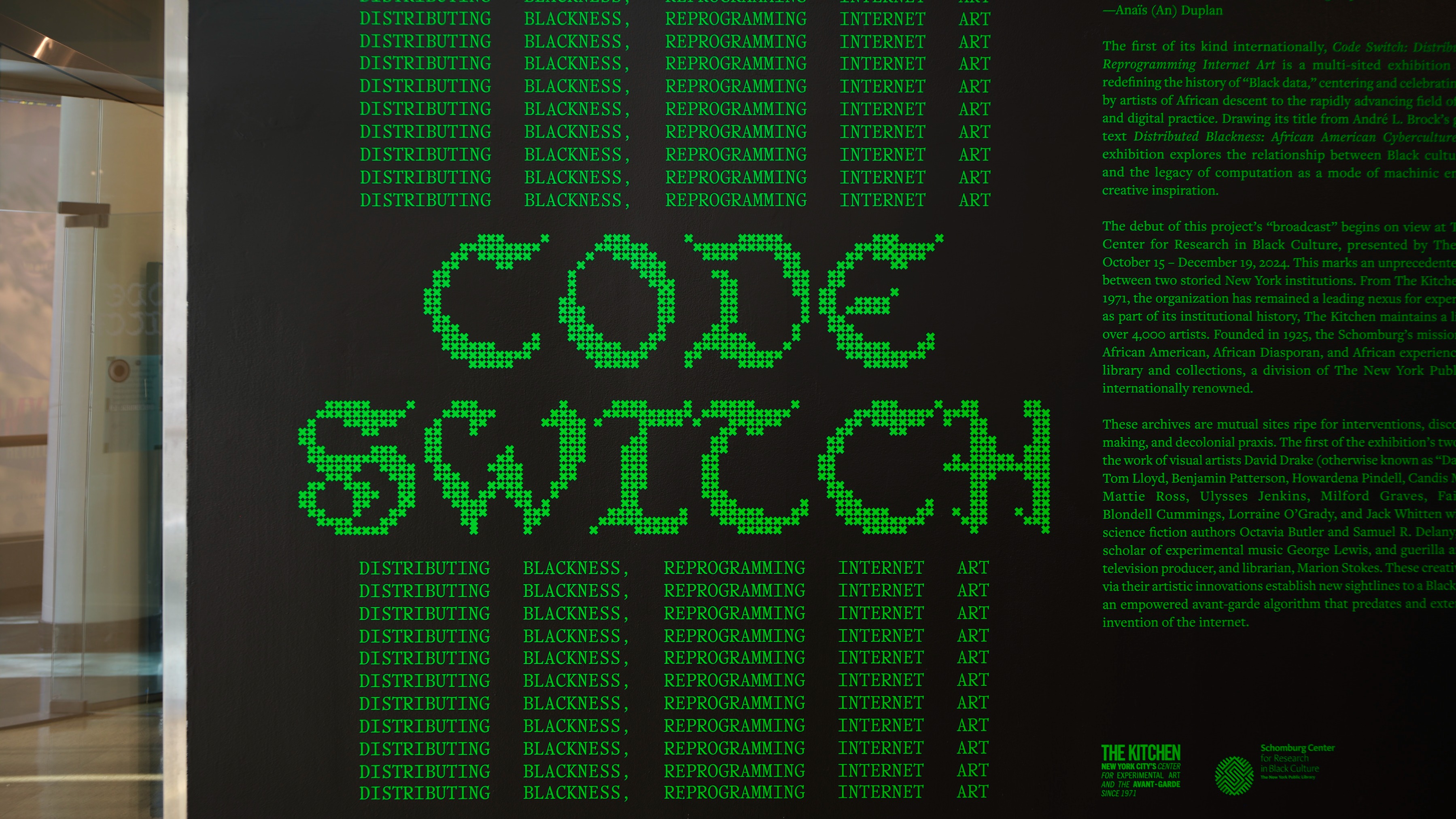 Black wall with green pixelated text reading “CODE SWITCH.” Surrounding words repeat: “DISTRIBUTING BLACKNESS, REPROGRAMMING INTERNET ART.” Exhibition and program details are partially visible to the right.