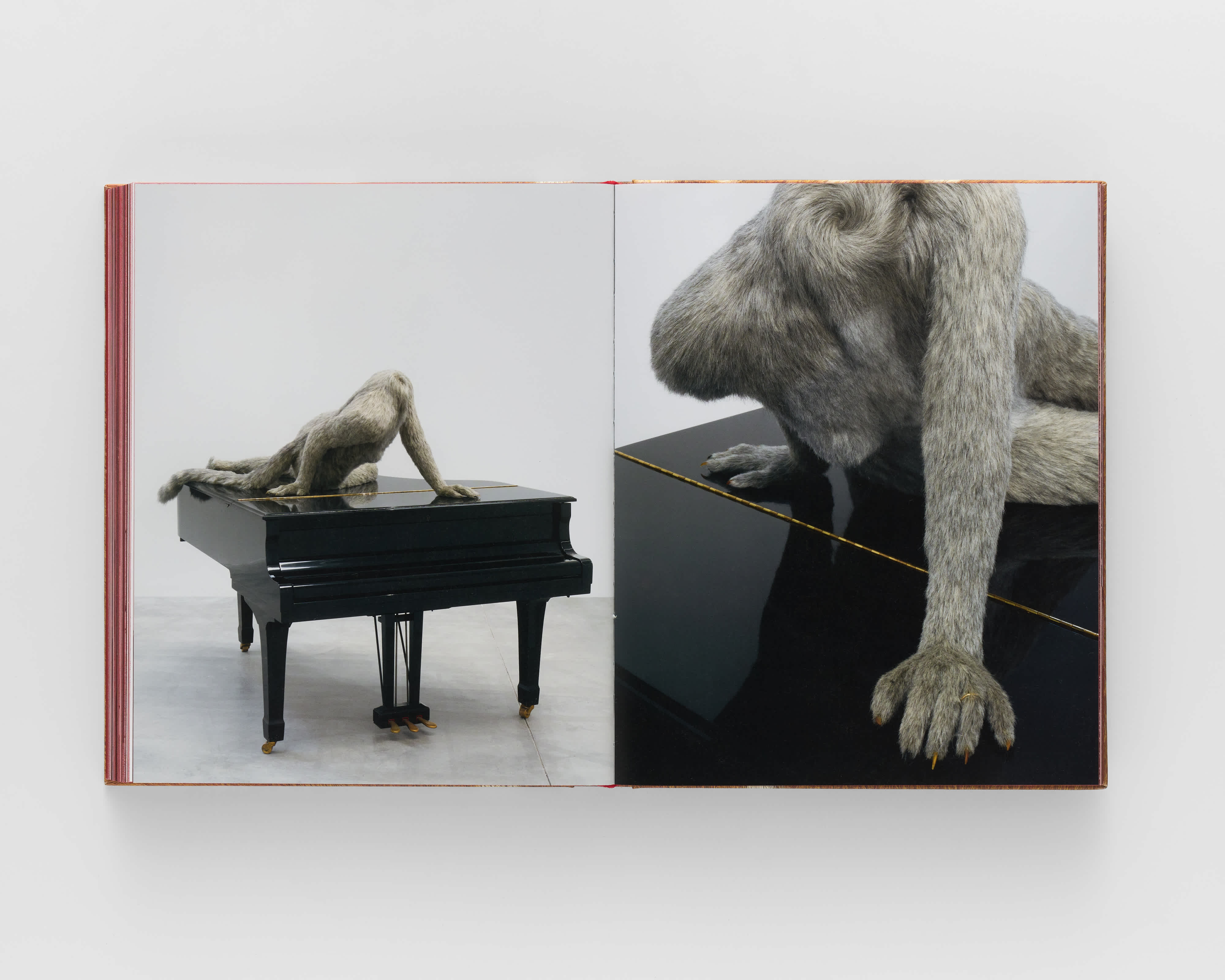 Open book with two photographs of the same sculpture on either page. The left page is a full shot which shows a fur-covered headless human body turning across a grand piano. The right page reveals the human figure to have claws for fingernails. 