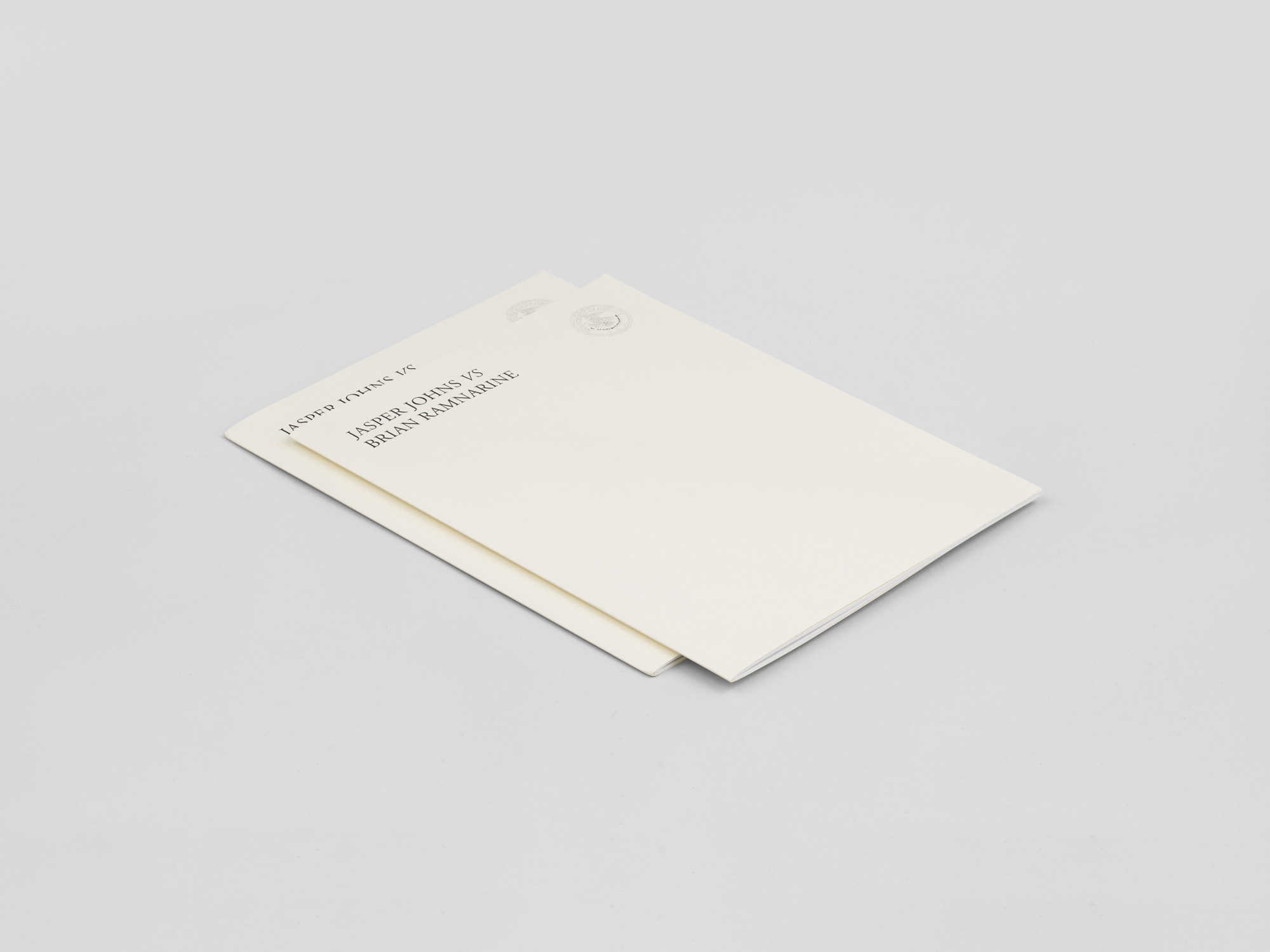 Two thin white books on top of each other, positioned diagonally in the frame.