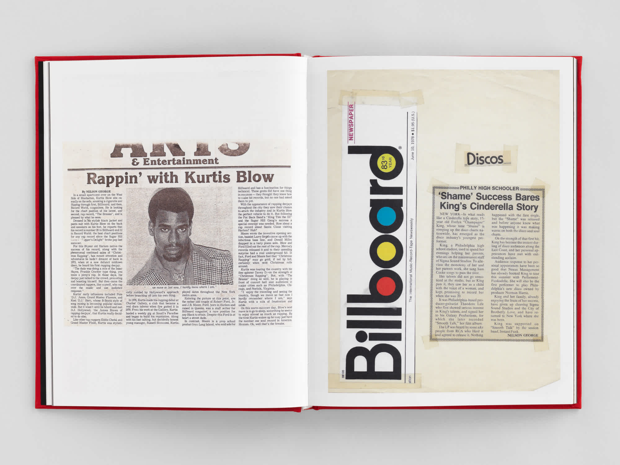 Open book. Each page has old newspaper clippings on it. The left page has a cutout from the arts and culture section with a picture of the rapper Kurtis Blow in the center, surrounded by text. The right page has a collage of newspaper clippings. 