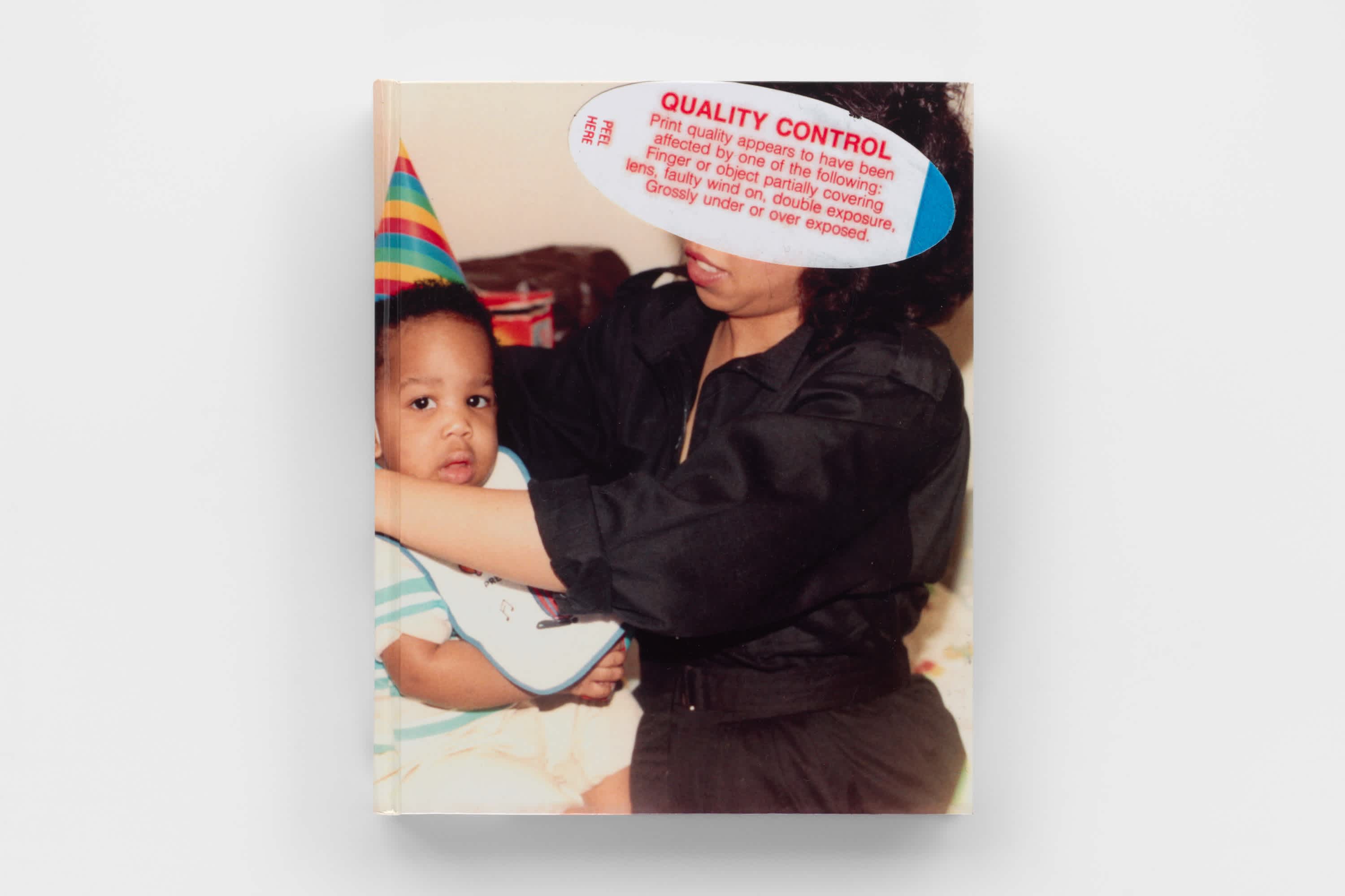 The front cover of a book floating on a gray background. The cover is an old home photo of a mother holding a baby. The baby wears a pointed birthday hat. The mother's face is obscured by a film processing quality check sticker which includes the title of the book, "Quality Control".