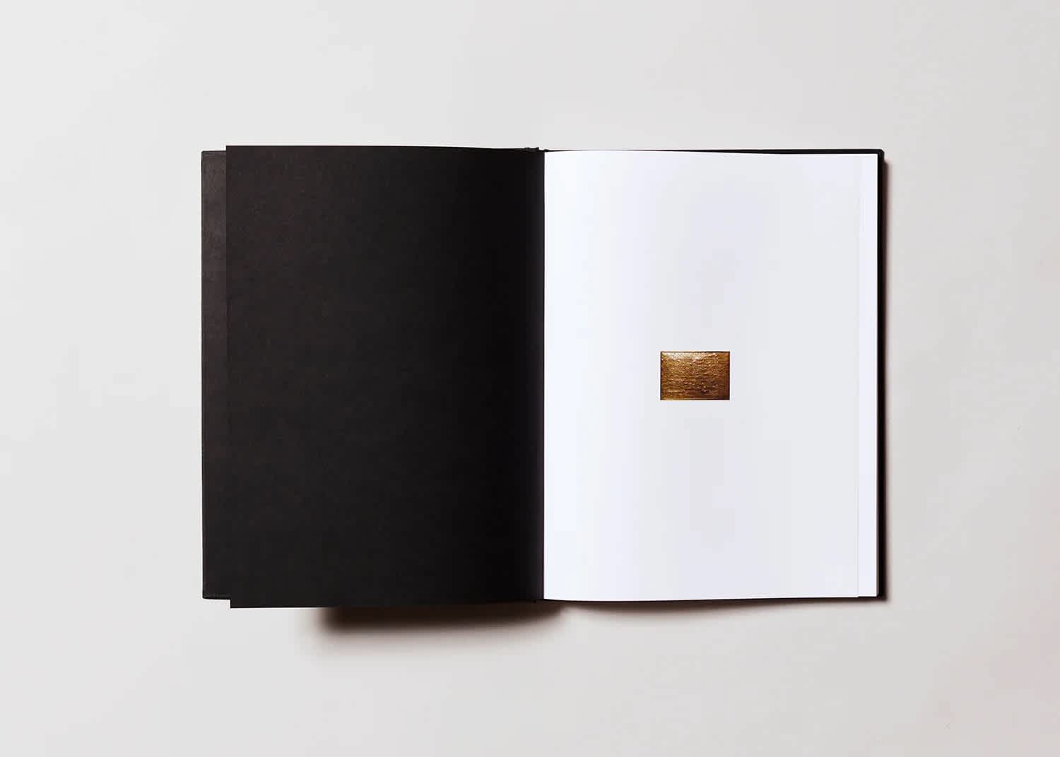 Open book with a blank, black left page and a small photograph in the center of the right page. 