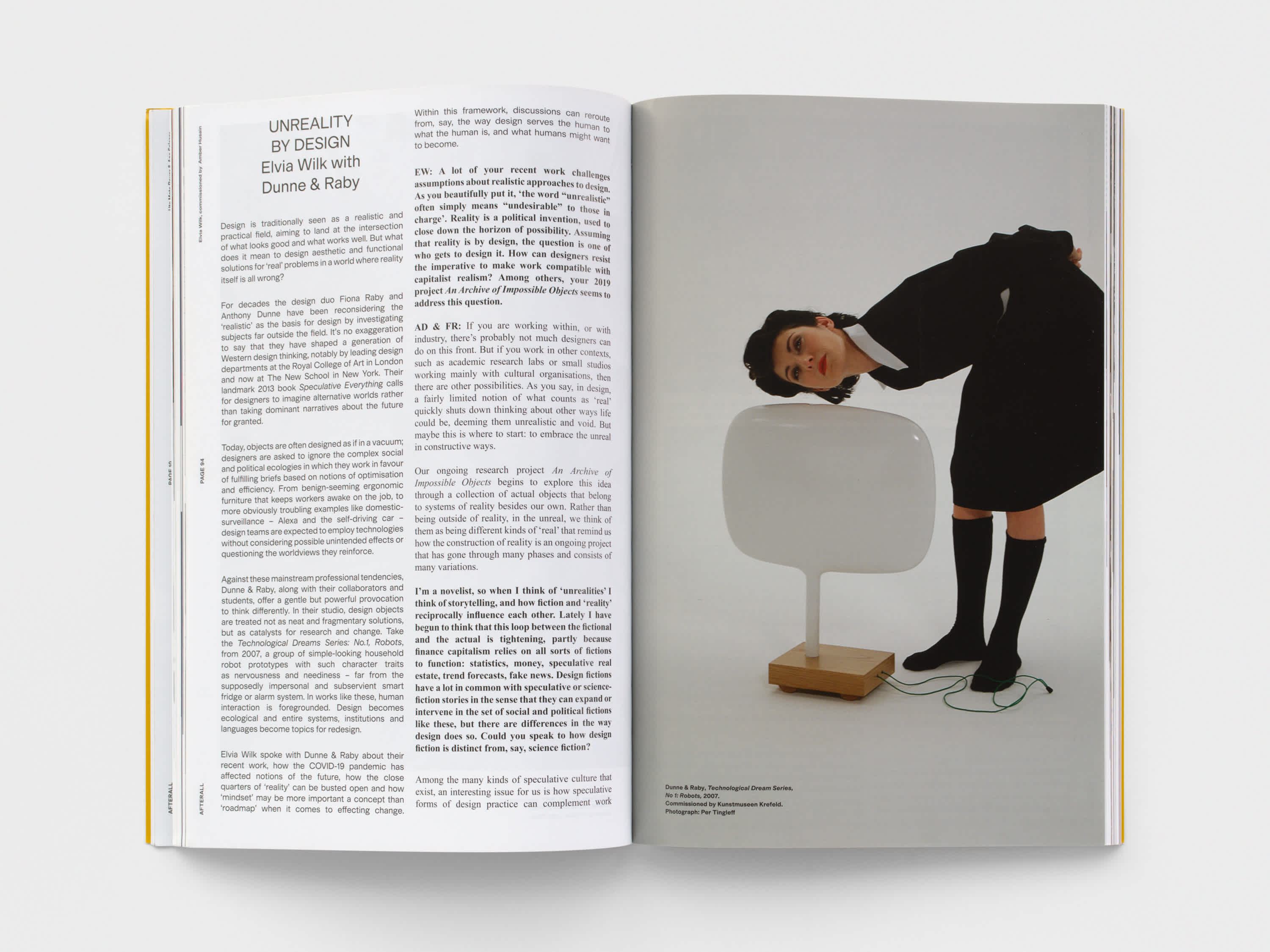 Open magazine with a text on the left page and an image on the right page. The woman in the image is wearing black clothing and bent at the waist and holds her ear up to a white futuristic lamp. 