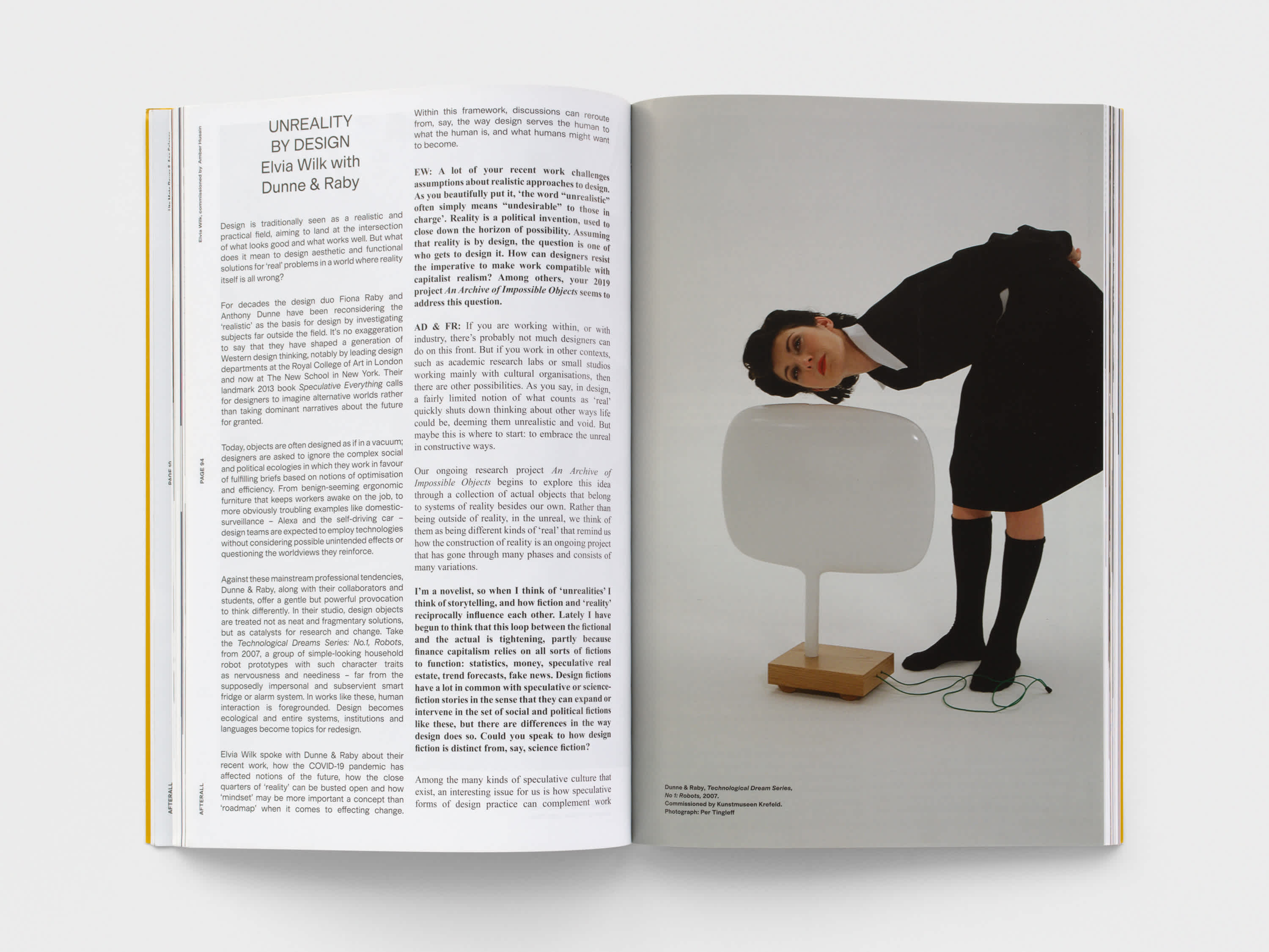 Open magazine with a text on the left page and an image on the right page. The woman in the image is wearing black clothing and bent at the waist and holds her ear up to a white futuristic lamp.