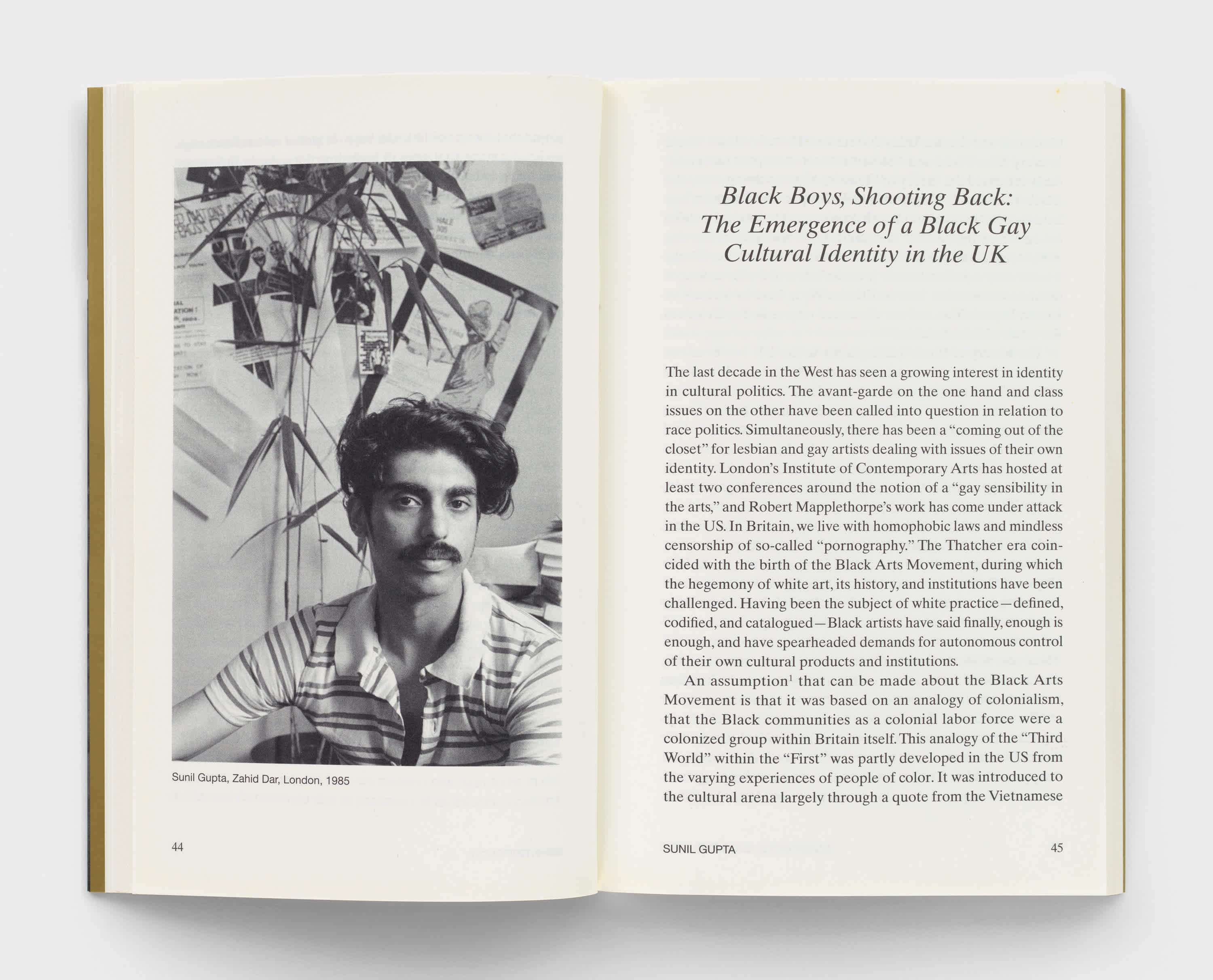 Open book with cream colored pages. A black and white photograph of a mustached man, wearing a striped shirt is on the left page. Essay text is on the right page. 