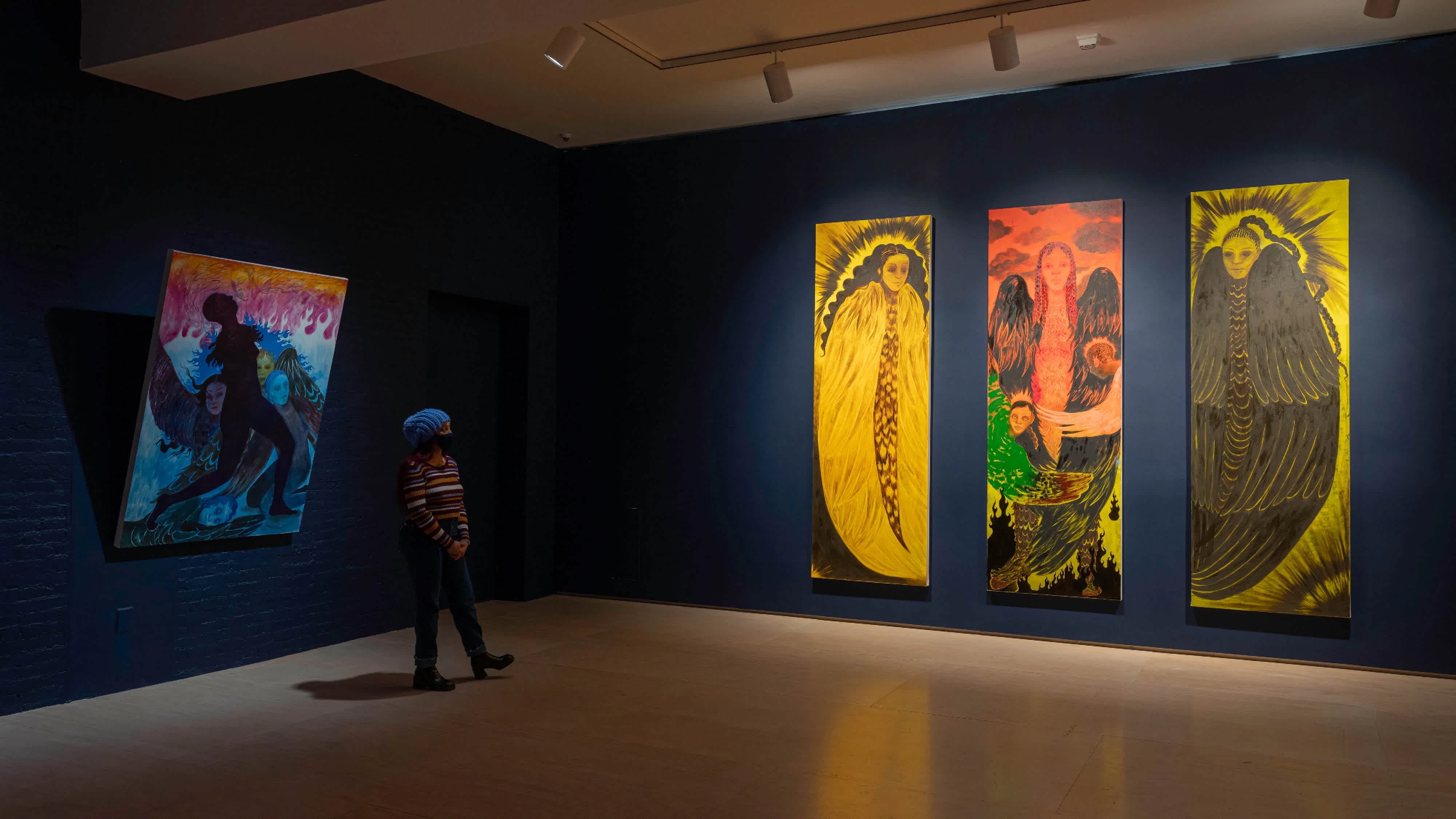 Exhibition shot with a person looking at artwork on the navy blue walls.