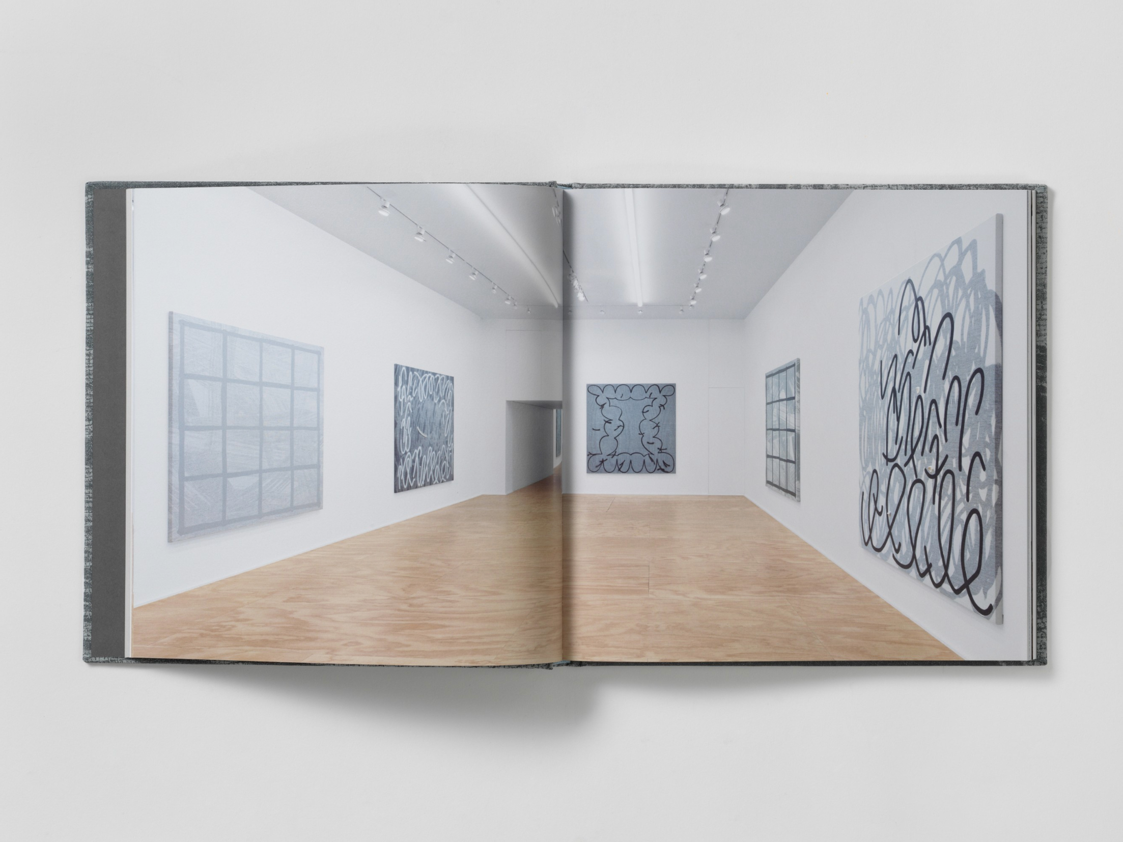 Interior of a book which has a full bleed, centerfold exhibition shot. There are several large paintings on the three visible walls.