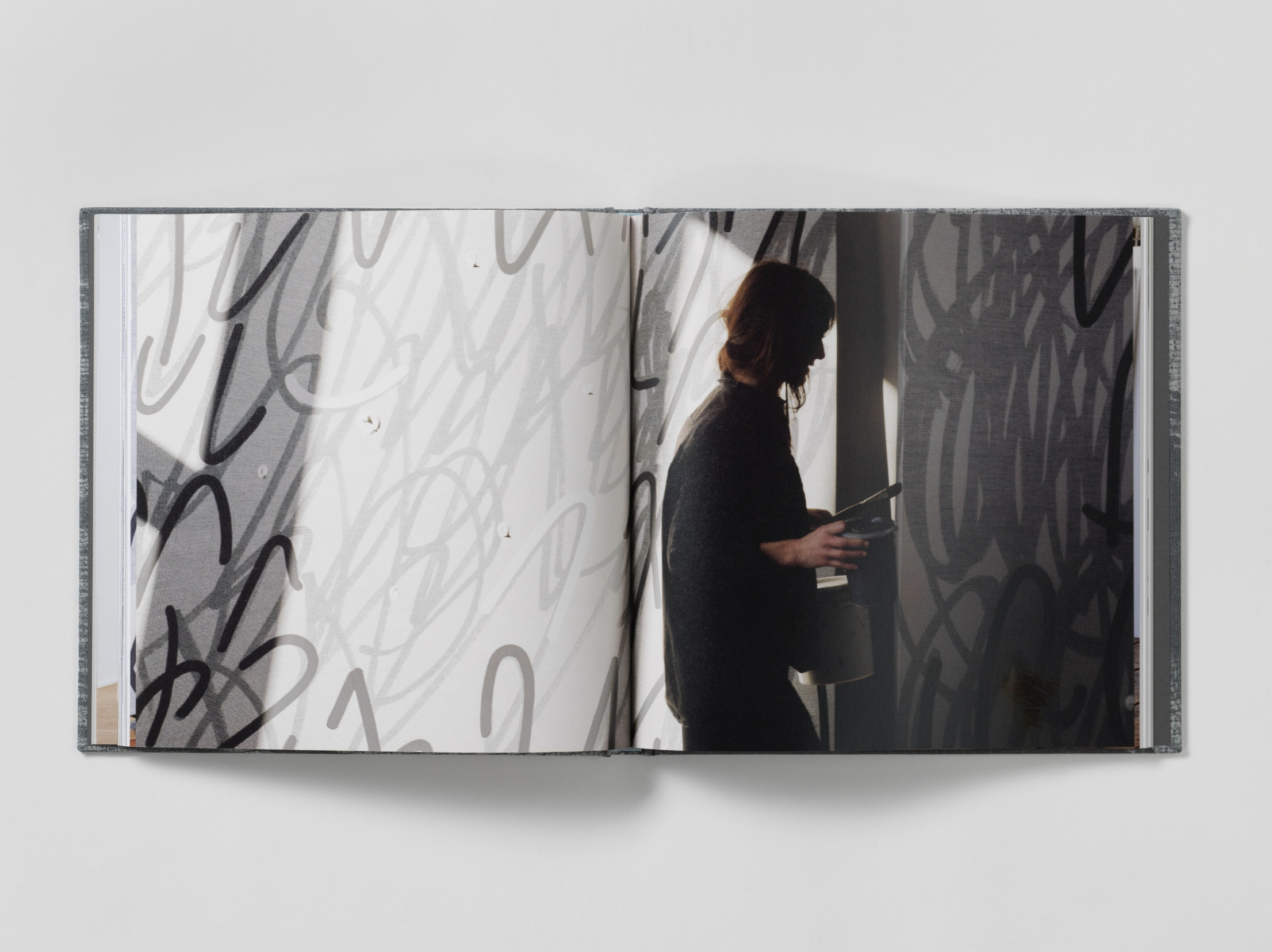 Interior of a book which has a full bleed centerfold of an artist painting a large scale gray painting.