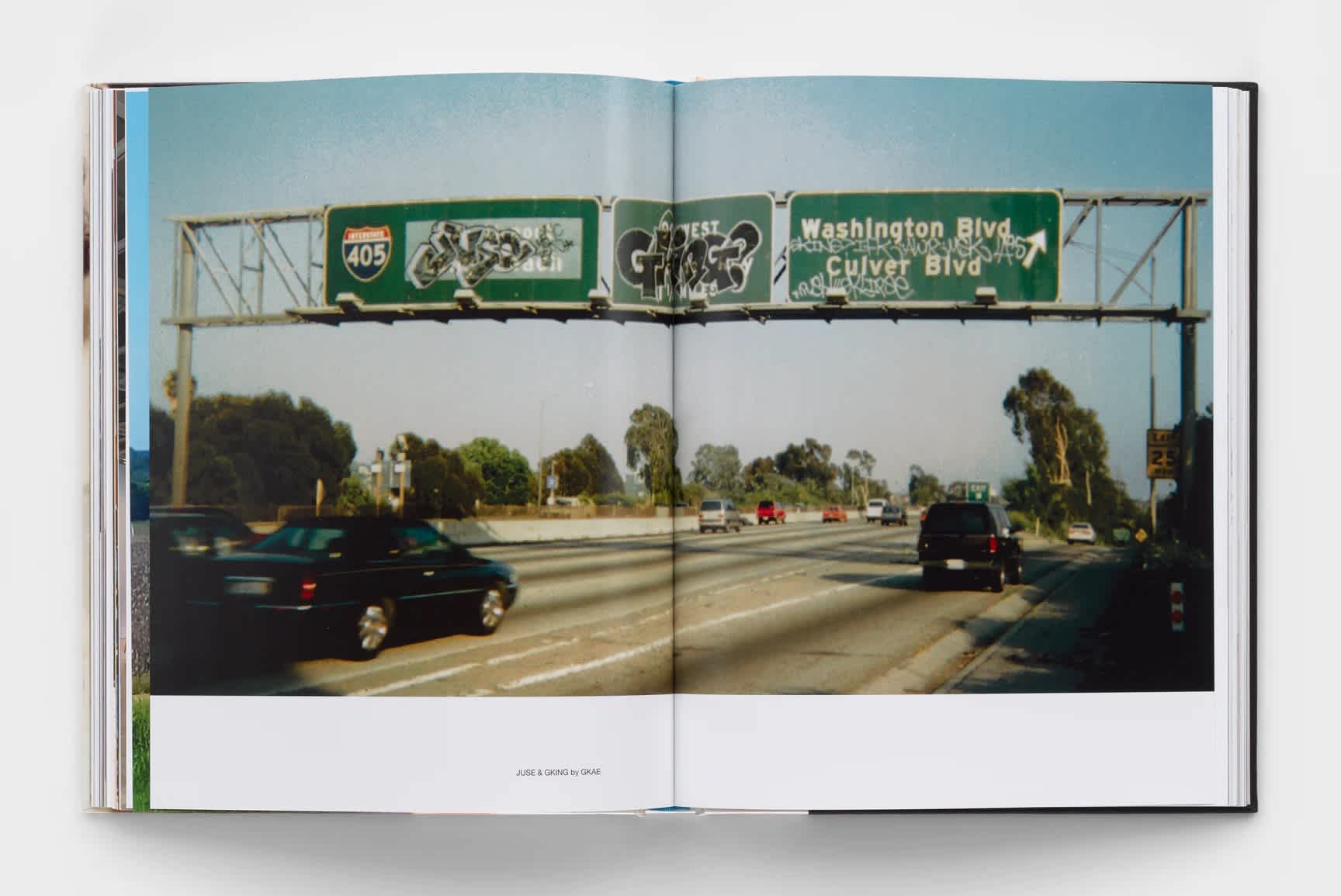 An old film photograph of a Los Angeles freeway sign covered in graffiti stretches across two pages inside of an open book.