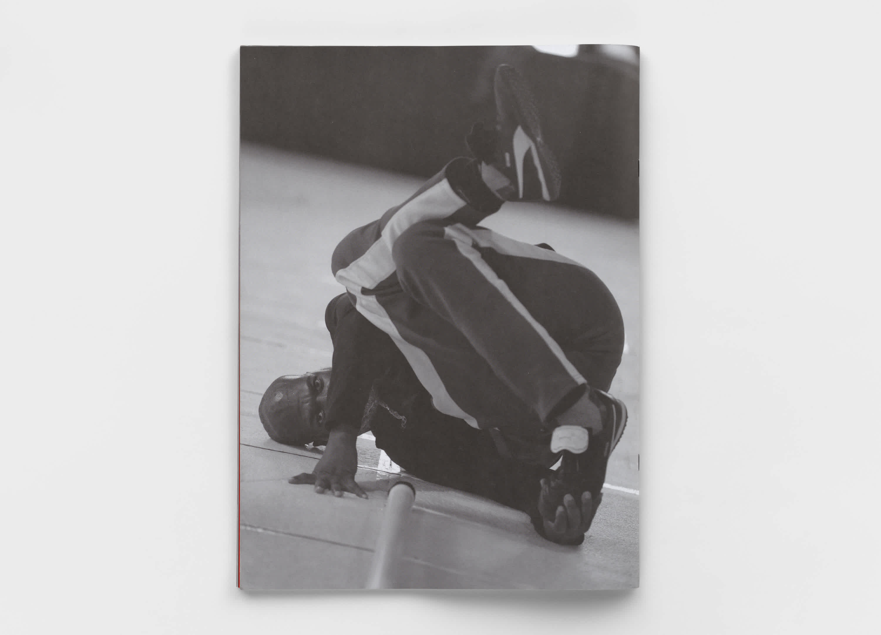 Back cover of a book in which a man in a track suit is bent into a precarious position on the floor, presumably dancing. The image is black and white. The book is on top of a light gray background.